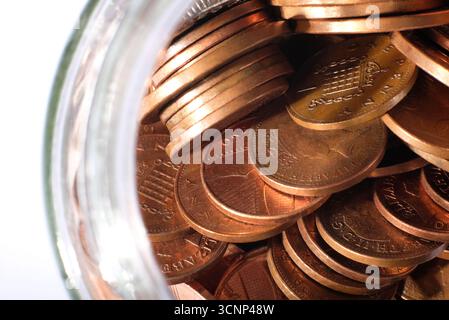 monete da penny inglesi in vaso di vetro su sfondo bianco Foto Stock