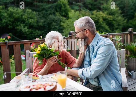 Figlio maturo che passa il tempo con la madre anziana, beve caffè e parla. Foto Stock