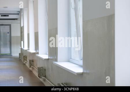 Lungo corridoio piastrellato. Corridoio vuoto con alte finestre che lasciano entrare la luce del giorno. Foto Stock