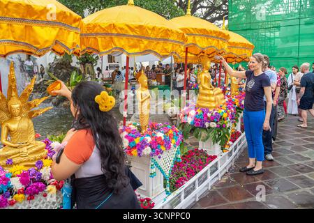 I turisti spruzzano acqua sulle statue di Buddha all'aperto, Wat Pho, Wat po, complesso di templi buddisti nel distretto di Phra Nakhon, Bangkok, Thailandia, Asia Foto Stock