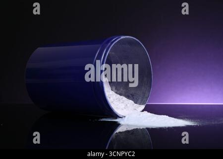 Prodotto cosmetico biondo per la cura dei capelli. Polvere in vasetto su piano nero su sfondo viola scuro, primo piano Foto Stock