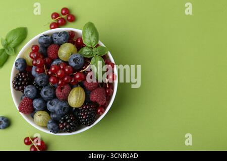 Diversi bacche mature e succose e basilico in ciotola su sfondo verde, piatto. Spazio per il testo Foto Stock