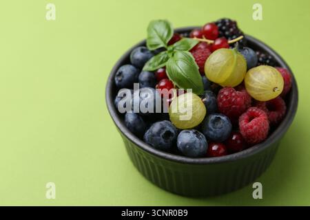 Diversi frutti di bosco e basilico maturi in ciotola su sfondo verde, primo piano. Spazio per il testo Foto Stock