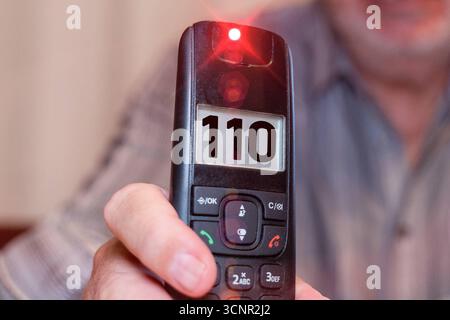 Germania - 21 settembre 2025: FOTOMONTAGGIO, un uomo anziano tiene un telefono con il numero di emergenza 110 sul display. L'immagine simboleggia una chiamata alla polizia in una situazione di emergenza *** FOTOMONTAGE, Ein älterer Mann hält ein Telefon in der Hand, auf dessen display Die Notrufnummer 110 erscheint. DAS Bild steht symbolisch für einen Anruf bei der Polizei in einer Notsituation Foto Stock