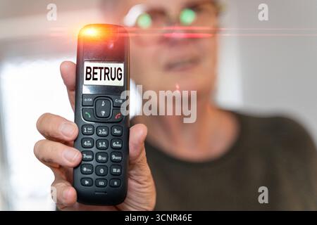 Germania - 21 settembre 2025: FOTOMONTAGGIO, una donna anziana tiene in mano un telefono. Sul display viene visualizzata la parola: Frode. Foto simbolo, frode telefonica e pericoli di chiamate fraudolente *** FOTOMONTAGE, Eine Ältere Frau hält ein Telefon in der Hand. Auf dem display erscheint das Wort: Betrug. Symbolfoto, Telefonbetrug und die Gefahren durch betrügerische Anrufe Foto Stock