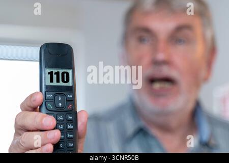 Germania - 21 settembre 2025: FOTOMONTAGGIO, un anziano chiama il numero di emergenza 110 sul suo telefono in preda al panico. Foto simboliche, paura e impotenza in una situazione minacciosa e il rapido allarme della polizia *** FOTOMONTAGE, Ein älterer Mann wählt panisch die Notrufnummer 110 auf seinem Telefon. Symbolfoto, Angst und Hilflosigkeit in einer bedrohlichen situation und die schnelle Alarmierung der Polizei Foto Stock