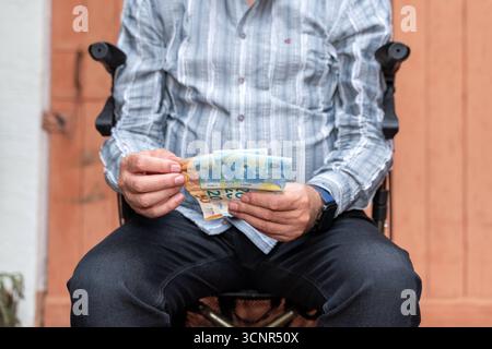 Germania - 21 settembre 2025: Un uomo anziano con un camminatore conta le banconote. L'immagine simboleggia l'attuale dibattito sulla riforma dell'assistenza sanitaria, l'aumento dei costi dell'assistenza e la questione di un sostegno adeguato per gli anziani e i loro parenti. *** Ein älterer Mann mit Rollator zählt Geldscheine. DAS Bild symbolisiert die aktuelle Debatte um Pflegereform, steigende Pflegekosten und die Frage nach ausreichender Unterstützung für Senioren und Angehörige. Foto Stock