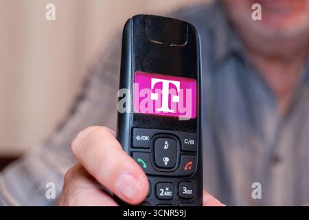 Germania - 21 settembre 2025: FOTOMONTAGGIO, un anziano possiede un telefono fisso con il logo del fornitore di telefonia mobile Deutsche Telekom *** FOTOMONTAGE, Ein älterer Mann hält ein Festnetz Telefon in der Hand mit dem Logo vom Mobilfunk und Telefonanbieter Deutsche Telekom Foto Stock