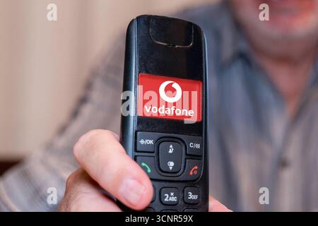 Germania - 21 settembre 2025: FOTOMONTAGGIO, un anziano tiene in mano un telefono fisso con il logo del fornitore di telefonia mobile Vodafone *** FOTOMONTAGE, Ein älterer Mann hält ein Festnetz Telefon in der Hand mit dem Logo vom Mobilfunk und Telefonanbieter Vodafone Foto Stock
