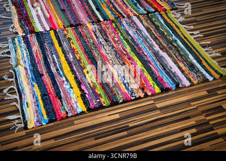 Vivaci tappeti in tessuto a mano multicolore disposti su pavimento in parquet scuro in un accogliente ambiente interno Foto Stock