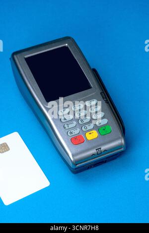 Terminale di pagamento e carta di credito bianca su sfondo blu Foto Stock