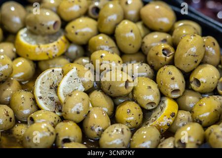 Primo piano di olive verdi marinate con fette di limone ed erbe aromatiche. Antipasto e snack mediterranei tradizionali, conditi con spezie e olio d'oliva Foto Stock