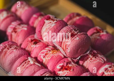 Primo piano di macaron rosa disposti in righe. Dolce dolce francese con ripieno di panna, decorato con glassa bianca e briciole. Colorato e discreto Foto Stock