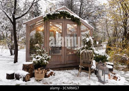 Una magica serra in legno ricoperta di neve e decorata con luci natalizie, annidata in una tranquilla foresta invernale Foto Stock