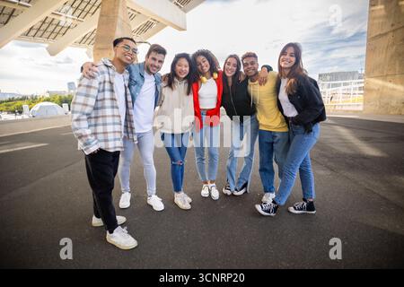 Un gruppo giovane e variegato di amici sorridenti alla macchina fotografica all'aperto Foto Stock