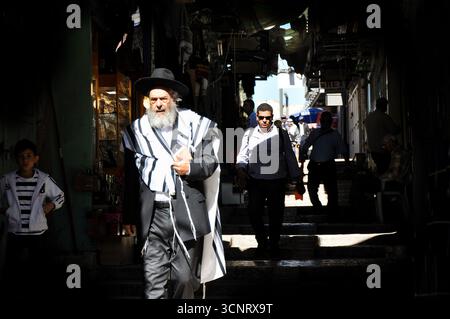 Uomo ebreo ortodosso che cammina attraverso i vicoli stretti della città vecchia di Gerusalemme, vestito con abiti tradizionali. Atmosfera storica e spirituale. Foto Stock