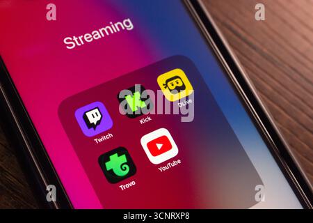 Primo piano di uno smartphone che visualizza una cartella intitolata "streaming" con le icone delle app di live streaming più diffuse: Twitch, Kick, DLive, Trovo e YouTube. Foto Stock