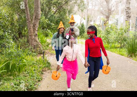 Due ragazze afroamericane che camminano sul sentiero del parco trasportando secchi di zucca in costumi di Halloween Foto Stock