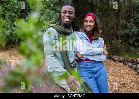 Coppie diverse sedute su una grande roccia nella foresta con sciarpa verde, fascia rossa con pelo di tronchi Foto Stock