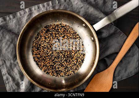 Semi di sesamo bianco e nero tostati in uno Skillet: Miscela di semi di sesamo tostati in una piccola padella in acciaio inox con una spatola di legno Foto Stock
