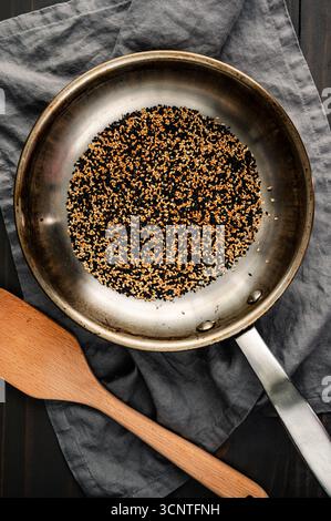 Semi di sesamo bianco e nero tostati in uno Skillet: Miscela di semi di sesamo tostati in una piccola padella in acciaio inox con una spatola di legno Foto Stock