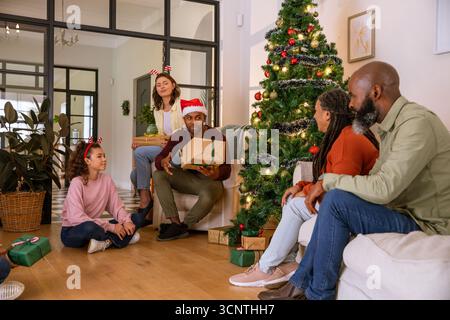 Diverse famiglie in cappello di babbo natale e abbigliamento festivo che scambiano regalo con l'albero di natale nel soggiorno Foto Stock