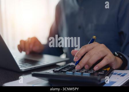 Contabile che lavora con le mani utilizzando la calcolatrice e il laptop. pianificazione finanziaria aziendale alla scrivania con documenti fiscali finanziari, fattura, penna e tecnico tecnologico Foto Stock