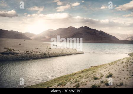 Una vista mozzafiato del Lago Pangong a Ladakh, India, con la luce del sole che illumina le aride montagne e le calme acque blu. Foto Stock