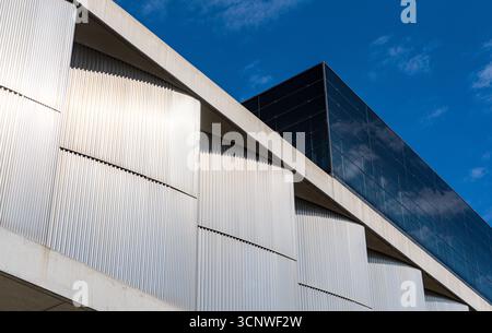 Vista dettagliata di una moderna struttura architettonica che presenta eleganti pannelli in vetro e superfici in cemento testurizzato, creando un contrasto dinamico sotto una cl Foto Stock