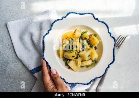 Una vivace insalata greca di patate con patate bollite, capperi piccanti ed erbe fresche. Servito in un piatto decorativo, perfetto per un pasto mediterraneo Foto Stock
