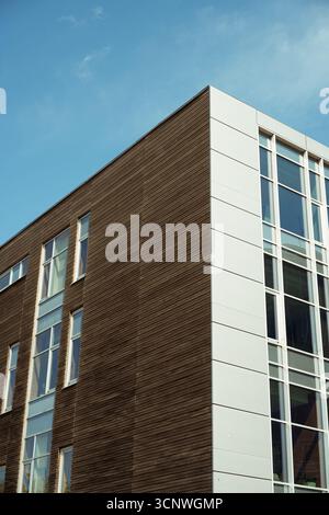 Vista ad angolo basso di un edificio moderno con facciata in legno e vetro, che mostra design e architettura contemporanei su un cielo blu chiaro, enfatizzando Foto Stock