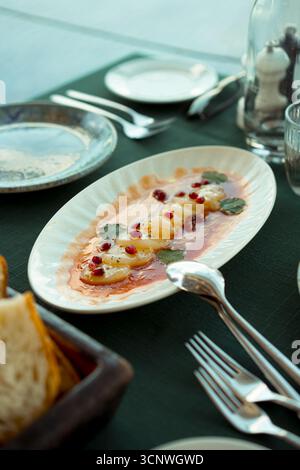 Un ceviche di capesante splendidamente placcato con semi di melograno ed erbe fresche è esposto elegantemente su un tavolo da pranzo, pronto per essere sa Foto Stock