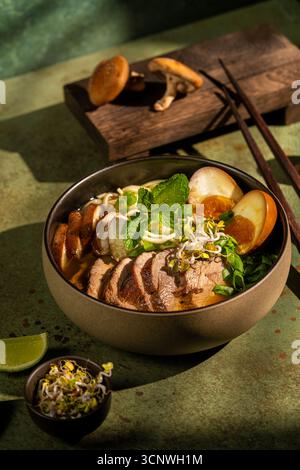Una ciotola di delizioso ramen d'anatra servito con noodle d'uovo, condita con funghi shiitake, menta fresca e germogli. Lo sfondo presenta un'avidità rustica Foto Stock
