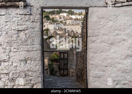 Un'incantevole vista attraverso un arco in pietra ad Alberobello, in Puglia, che rivela le iconiche case dei trulli imbiancate con tetti conici, annidate tra lussureggianti Foto Stock