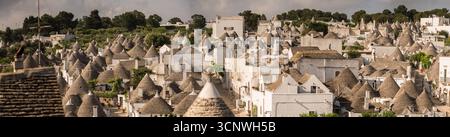 Vista panoramica delle tradizionali case dei Trulli ad Alberobello, Puglia, Italia. Queste storiche strutture in pietra con tetti conici sono annidate sotto un trasparente Foto Stock