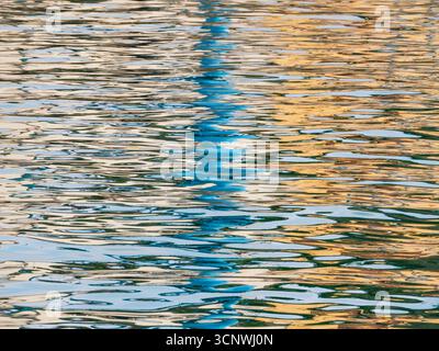 Questa immagine cattura una scena serena di riflessi di luce e colore sull'acqua calma, creando un ipnotico gioco di simmetria visiva e effetto specchio Foto Stock