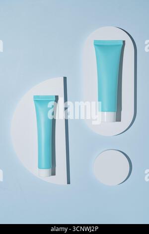 Confezione cosmetica minimalista su sfondo blu sereno con forme geometriche bianche. Ideale per temi di design moderno e prodotti per la cura della pelle p Foto Stock