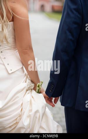 Una sposa e uno sposo si tengono per mano, simboleggiando l'unità e l'amore nel giorno del loro matrimonio. La sposa con un abito bianco e lo sposo con un abito condividono un look intimo Foto Stock