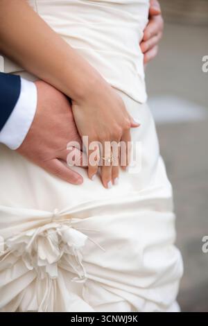 Un primo piano delle mani di una coppia sposata che mostra eleganti fedi nuziali. La mano della sposa si appoggia delicatamente sullo sposo, simboleggiando l'unità e l'amore Foto Stock