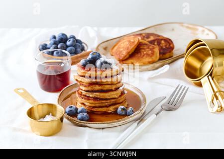 Una deliziosa pila di pancake conditi con mirtilli freschi e conditi con sciroppo. Accompagnato da un lato di mirtilli, sciroppo e meas dorati Foto Stock