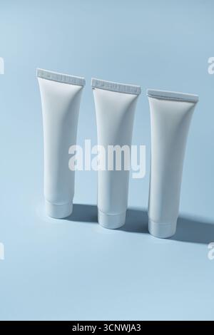 Tre tubi bianchi di crema cosmetica sono in posizione verticale su un morbido sfondo blu. Ideale per presentare prodotti per la cura della pelle in un ambiente minimalista e professionale Foto Stock