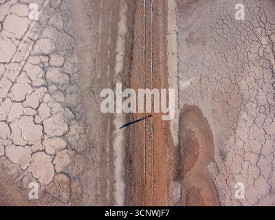 Vista aerea irriconoscibile di un uomo anonimo che cammina attraverso vaste distese saline incrinate, evidenziando motivi e texture naturali in un remoto, Foto Stock