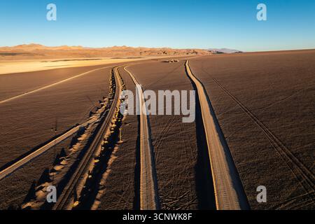 Vista aerea dei lunghi percorsi per veicoli che attraversano le vaste pianure desertiche di la Puna nel nord dell'Argentina. Paesaggio remoto ad alta quota con mountai Foto Stock