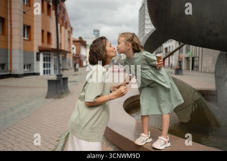 Un momento emozionante, mentre madre e figlia condividono un bacio dolce mentre si trovano vicino a una fontana della città. Entrambi tengono il gelato, godendosi un giocoso e lo Foto Stock