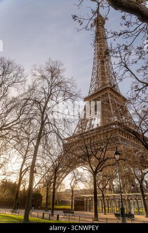 Una tranquilla scena mattutina con la Torre Eiffel incorniciata da alberi senza foglie. La luce dorata emette una calda luce soffusa, creando un'atmosfera tranquilla nella Foto Stock