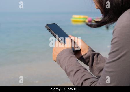 Foto con vista laterale di una donna sulla spiaggia che legge un messaggio di testo su uno smartphone con spazio per le copie. Foto Stock