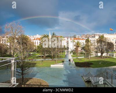 Parco urbano con arcobaleno a Santander - Un vibrante arcobaleno su un parco cittadino a Santander, caratterizzato da lussureggianti prati verdi, palme e classica Spa Foto Stock