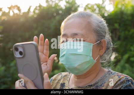 Salute, sicurezza e concetto pandemico - donna anziana felice che indossa maschera medica per la protezione dal virus con smartphone al parco estivo. Foto Stock