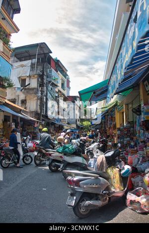 Vivace strada del mercato con moto e venditori ambulanti - Una foto verticale di una strada trafficata e stretta piena di moto parcheggiate, colorate facciate di negozi, e. Foto Stock