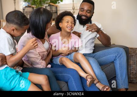 Diverse famiglie sedute su un divano grigio nel soggiorno, padre solletico, figlia e madre che guardano Foto Stock